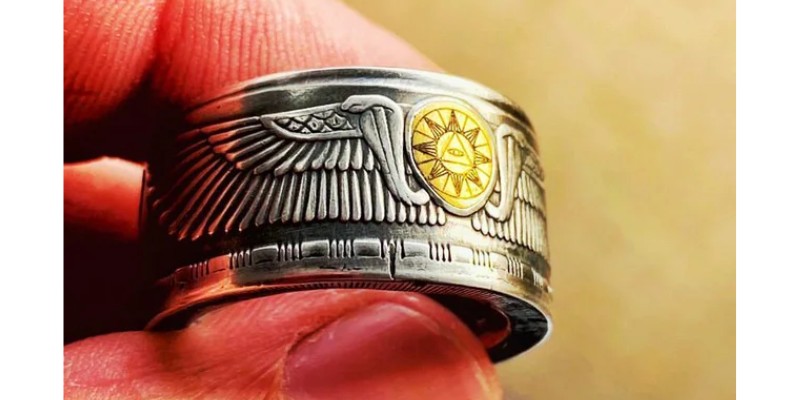 A silver Egyptian coin ring with a gold inlay that has a laser etched design.